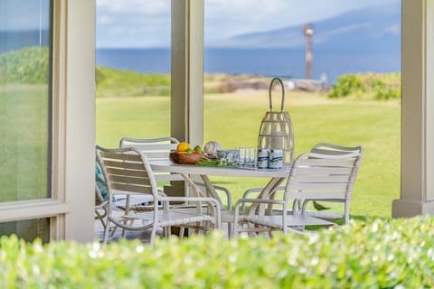 Outdoor dining area with a white patio table and chairs overlooking a lush green lawn and ocean view.