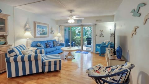 Coastal-themed living room with blue striped seating and natural light from sliding glass doors.