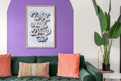Colorful living area with a green velvet sofa, vibrant pillows, Dolly-inspired wall art, and modern décor.

STR Permit # 2021028383