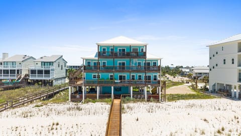 A beachfront property featuring direct access via a wooden walkway stretching across pristine white sand and coastal dunes to the shoreline.