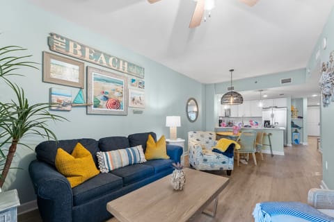 Relax in your coastal-themed living space with beach artwork, comfortable seating, and an open kitchen perfect for vacation dining.