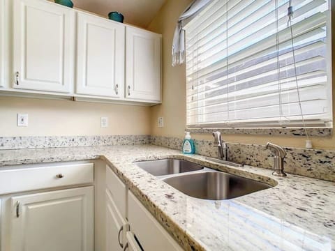 Our clean kitchen with white cabinets and granite countertops. A double sink sits beneath a window with blinds.