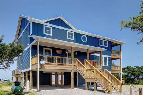A distinctive blue beach house on stilts features wraparound porches and wooden stairs, perfectly positioned for coastal getaways.