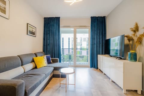 A bright and spacious living area featuring a gray sofa, vibrant yellow pillows, and a dining table in a contemporary setup.