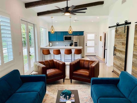 Bright open plan living room with velvet sofas, leather chairs, gold pendant lights and bright kitchen cabinets