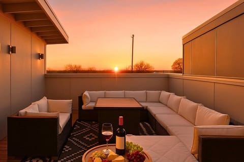 Rooftop terrace at sunset with a sectional sofa, fire-pit table, and stunning evening views