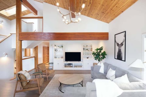 - Open-concept living room with high wooden ceilings and warm natural light  
- Cozy seating area with TV, modern décor, and elegant forest-inspired touches  
- Perfect mountain cabin vibe for relaxing after a day of outdoor adventures  
