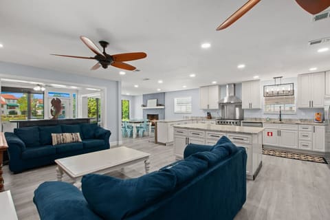 A full view of an open kitchen and spacious living room, featuring two blue couches, a TV, and sliding glass doors that lead to the backyard, offering a wonderful view, all in a bright and airy space.