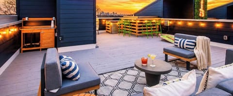 String lights glow over the rooftop bar area with cornhole and green seating as the city skyline glows during sunset, the perfect stage for a group celebration in Nashville