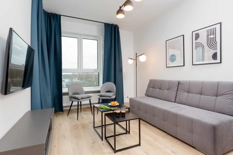 A comfortable living room featuring a stylish gray sofa, a sleek flat-screen TV on a wooden stand, and a minimalist coffee table. Perfect for unwinding in a calm and neutral space.