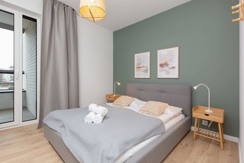 A cosy, bright bedroom with a double bed with grey headboard. One of the walls is in green which adds a unique touch.