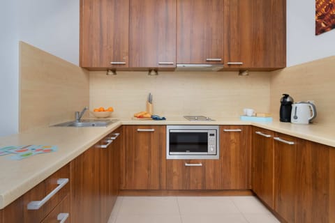 A modern kitchen setup with wooden cabinets, a stainless steel microwave, and a stovetop. The area also includes a countertop with a small fruit bowl.