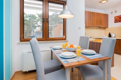 A dining area with a gray dining table and chairs. The room features large windows with bright blue curtains and a light-filled ambiance.