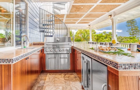 Outdoor kitchen with professional grill, refrigerator, and icemaker.
