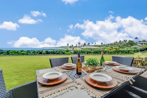 Oceanview lawn dining area with a woven outdoor table and seating, perfectly positioned to enjoy al fresco meals, tropical breezes, and sweeping views of blue skies and rolling greenery.