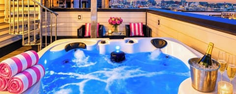 Hot tub with striped pillow chairs and city lights below creates the kind of rooftop moment that makes group trips unforgettable