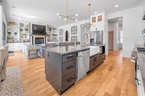 This view features a stylish kitchen island and cozy living room. Modern décor, warm lighting, and spacious design create a perfect setting for cooking, dining, and relaxing together.