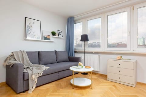 A bright living room with a gray sofa, a coffee table, and large windows letting in natural light.
