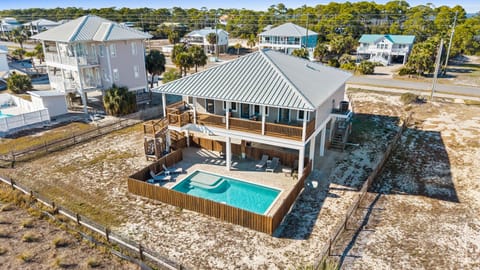 Aerial view showcases this coastal vacation home featuring private pool, elevated deck, and convenient beach access in a tranquil residential neighborhood.