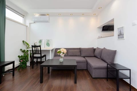 A spacious living room with a large L-shaped gray sofa, a coffee table, and modern decor. The room is well-lit with large windows and has a sleek, minimalist style.