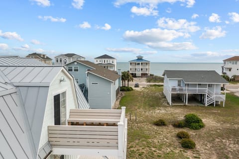 Elevated view from upper deck overlooking coastal homes, sandy lots, and the Atlantic Ocean in the distance, showcasing the beachside setting of this Oak Island vacation rental.