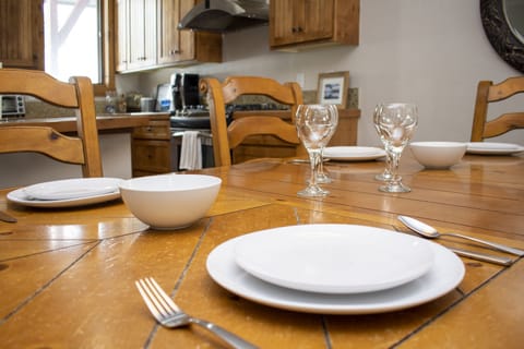 - Wooden dining table set for four with white dishes, bowls, and wine glasses - Perfect setting for cozy meals, game nights, or casual breakfasts at home - Open sightlines to the kitchen make this a great space for connection