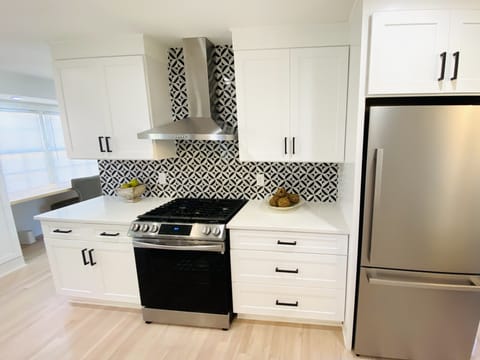 Renovated kitchen with marble backsplash, stainless appliances, and vent hood.