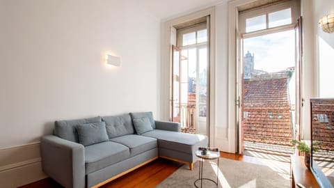 Unwind on the comfortable sectional sofa in this charming living room, where natural light pours in through the open balcony doors, offering a glimpse of historic rooftops and city life below. This inviting space is perfect for relaxing after a day of exp