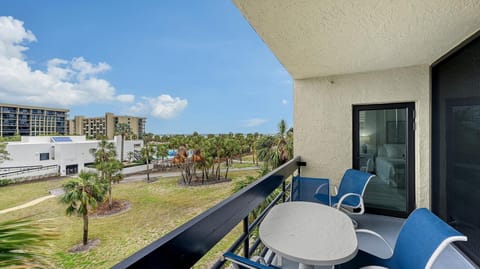 Second-floor balcony with textured cream walls, black railing, oval table, blue mesh chairs, and palm tree views.