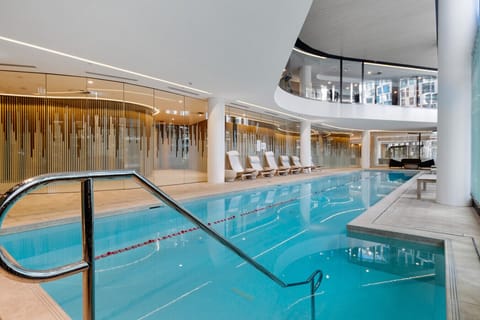 Indoor tepid lap pool on ground level with gym seen through glass windows on upper level 1.
