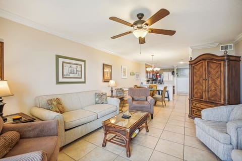 - Spacious living room with sofa seating, TV, and ceiling fan comfort  
- Open layout extends to dining and kitchen with coastal décor  
- Relaxing space to gather and enjoy ocean views from indoors
