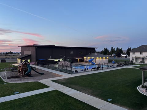 Evening view of the fenced outdoor pool area with blue slide, rock water feature, and shaded lounge seating.