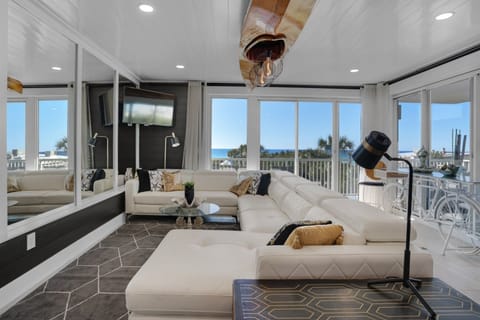 Relax in your bright coastal living room with plush white sectional seating and stunning ocean views through floor-to-ceiling windows.