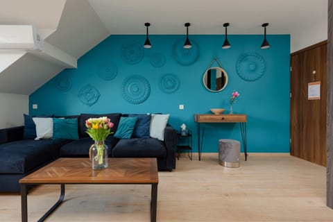 A modern living room with vibrant blue walls, a black sofa, a wooden coffee table, and stylish lighting fixtures.