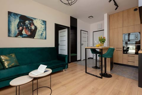 A cozy living room featuring a green sofa, a small round coffee table, and wall art for a modern touch. The wooden floors add warmth to the room's ambiance.