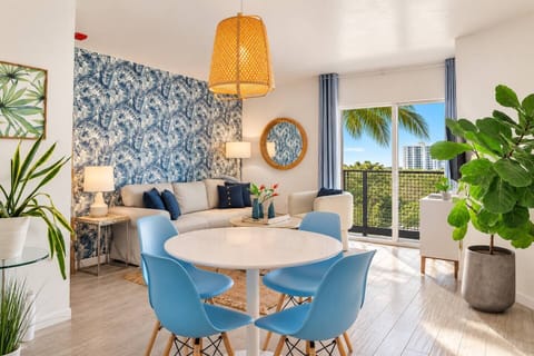 Eat breakfast at the white circular dining table, surrounded by four blue molded chairs in this bright Miami Beach space. A large woven pendant lamp and tropical leaf wallpaper add a mid-century-vibe to your morning meal.