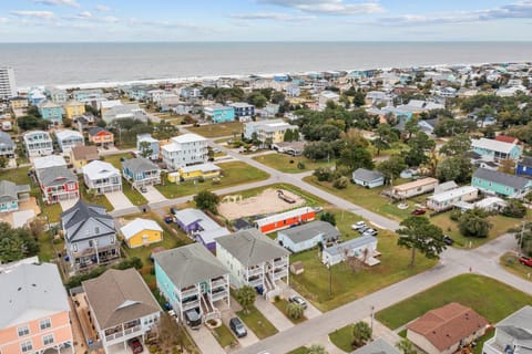 Aerial view of a charming coastal community with colorful beach houses nestled between tree-lined streets and the ocean shoreline.