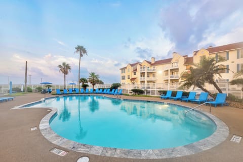 Beautiful pool area with tropical landscaping and multi-story resort buildings under a scenic sky.