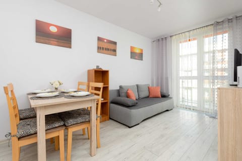 A living room with bright walls, a large sofa, a coffee table, and paintings on the wall. A spacious window allows a lot of natural light into the room.