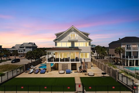 Stunning beach house at twilight featuring private pool, expansive outdoor living space, and coastal architecture in charming neighborhood setting.