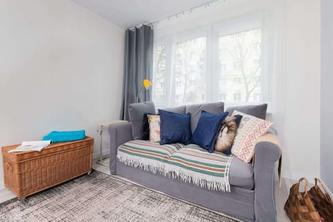 A living room with a cozy gray sofa, decorative cushions, a woven basket, and a large window letting in natural light.