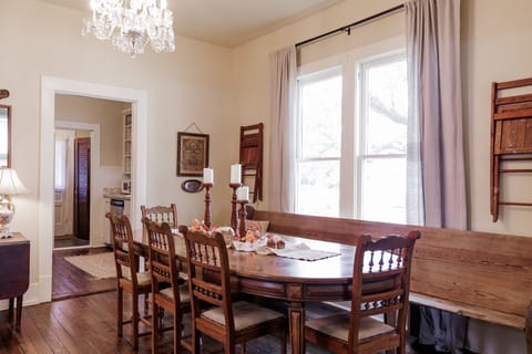 Dining room with antique table, chandelier, and church pew seating.