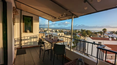 Spacious, covered terrace with a dining table, chairs, and decorative lighting. From here, you can enjoy sweeping views over the neighborhood rooftops, green treetops, and all the way to the sea. Ideal for al fresco dining or relaxing evenings at sunset. The terrace is partially covered, providing shade from direct sunlight while still allowing plenty of natural light to filter through.