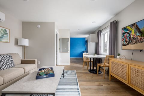 Bright open living area w/ cozy sofa, dining table & wood floors leading to a bold blue accent wall.