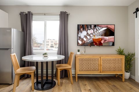 Intimate dining nook w/ round table, woven bench seating & wall-mounted TV for easy meals & movie nights.