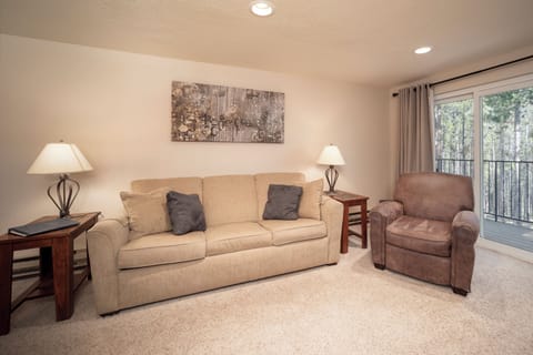 Unwind in your comfortable living space with plush seating and serene forest views through your private balcony doors.