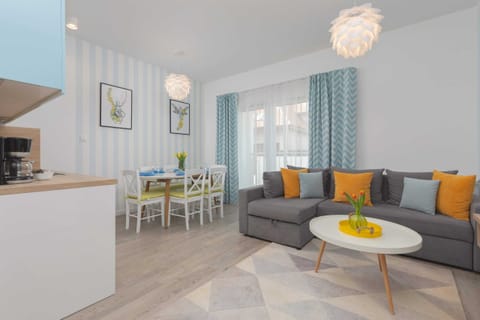 A modern living room featuring a cozy gray sofa, bright yellow cushions, and a sleek TV mounted on the wall. The large window allows plenty of natural light to brighten the space.