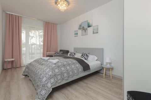 A cozy bedroom featuring a queen-sized bed with a patterned duvet. Soft pink curtains frame the window, creating a warm, inviting atmosphere.