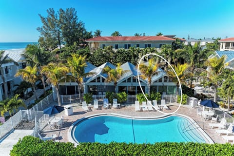 Tropical resort featuring pool area surrounded by lush palm trees with ocean views and multiple property buildings.
