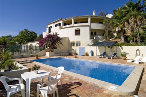 Villa Lorena's large pool is surrounded by a terrace with an outdoor shower and enough space for sun loungers or tables. A staircase leads up to the house.